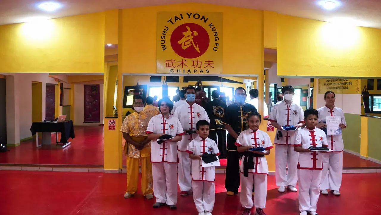 Alumnos de kung fu con uniforme blanco y rojo en el salón de la escuela Tai Yon